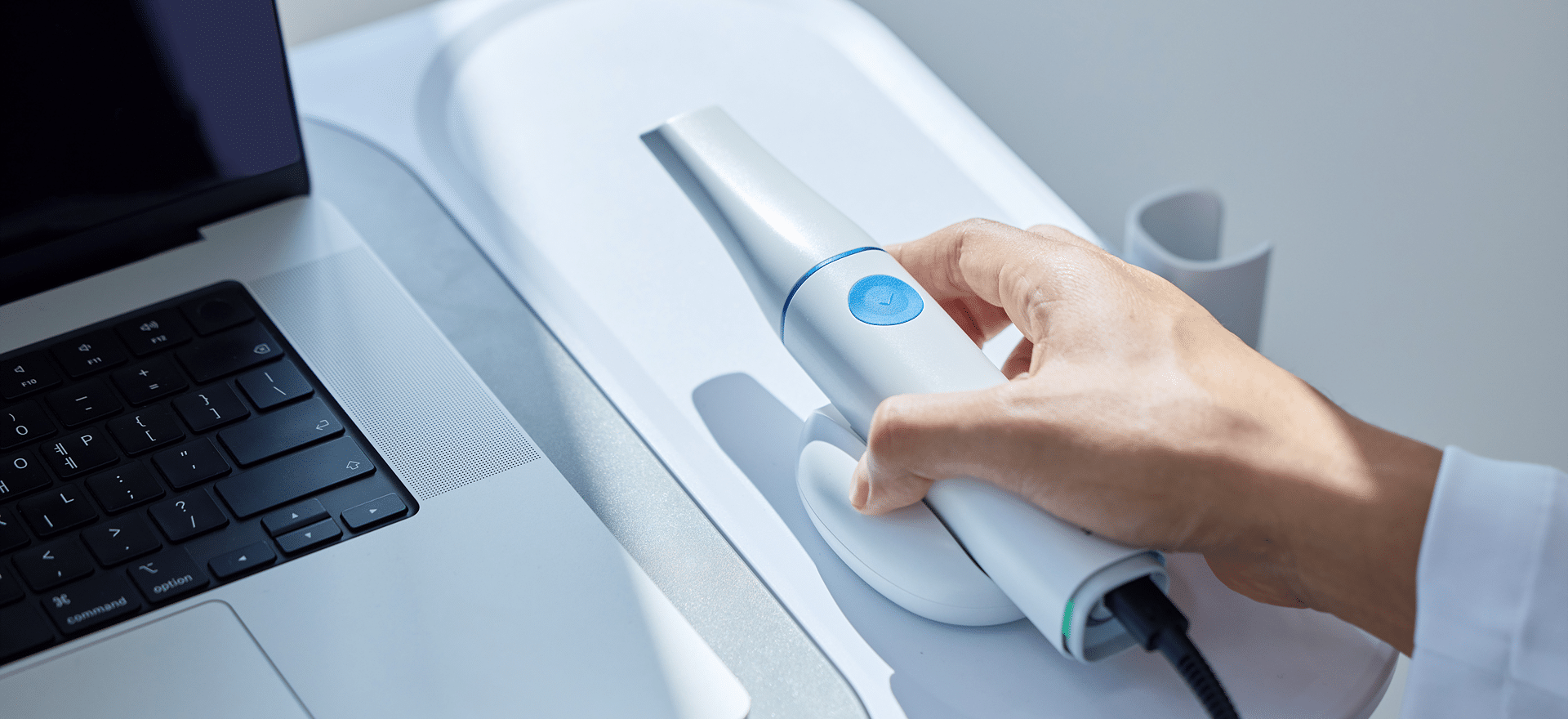 Hand mit einem Intraoralscanner, daneben ein Laptop, den man nur zur Hälfte sieht